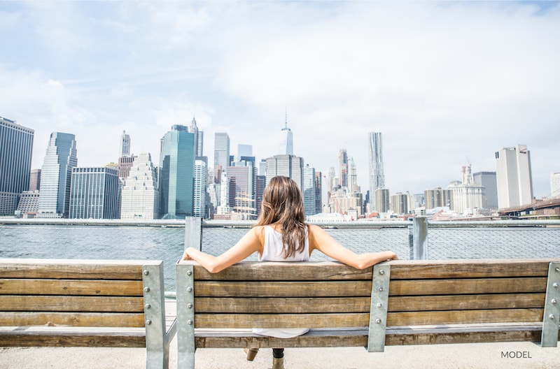 Woman sitting on a wooden bench looking out at the New York City skyline.