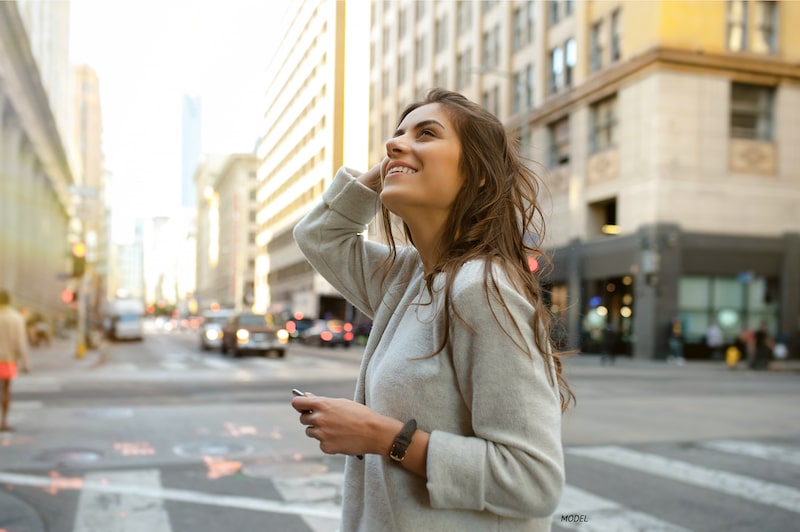 Young, happy woman looking up at a downtown city street.