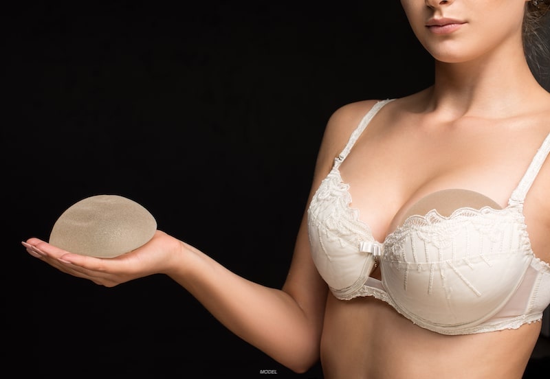 Woman holding breast implant in hand with another stuffed in her bra.