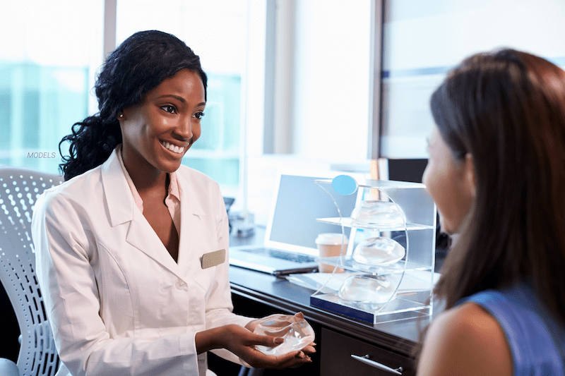 A female doctor shows a woman a breast implant.